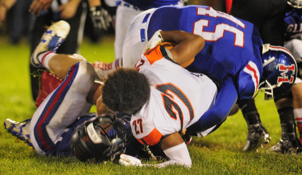 Brunswick's Ben Palizay, middle, loses his helmet while getting tackled by Messalonskee's Cameron Bickford, bottom, and Yan Gusmanov (45) during a Pine Tree Conference Class B game Friday at Veterans Field in Oakland.