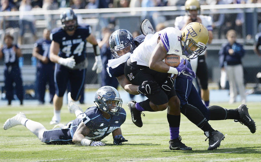 Maine defenders DeAndre Scott, left and Darius Greene, center, try and take down John Miller of James Madison during the first half Saturday in Orono.