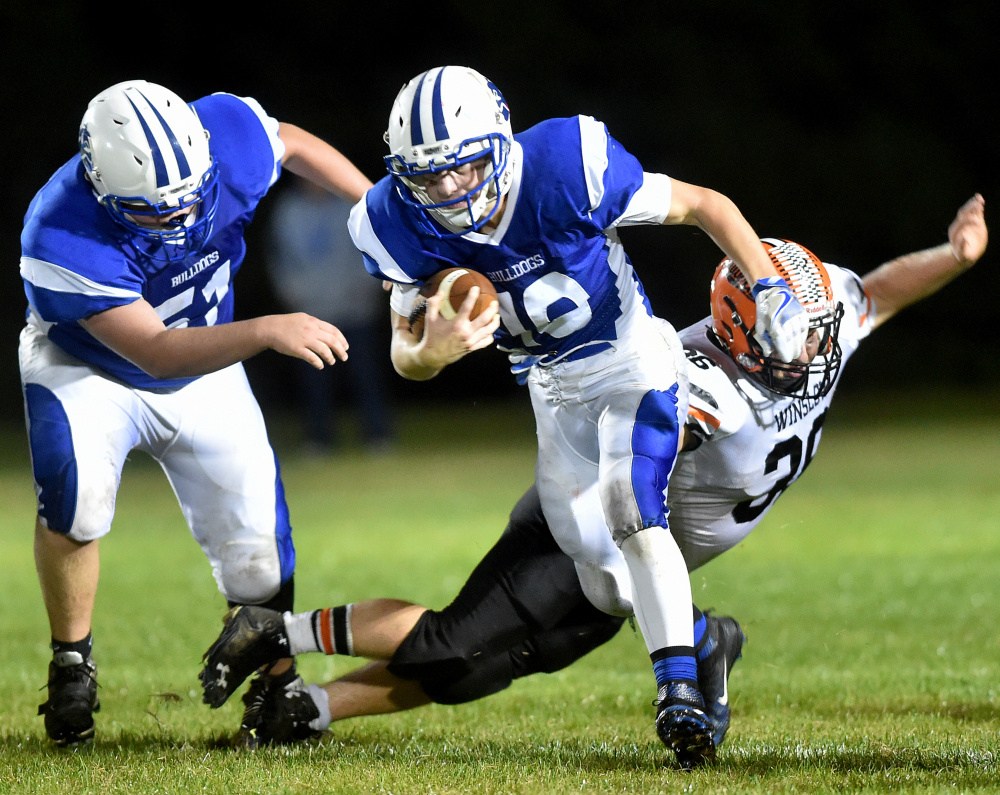 Madison quarterback Evan Bess evades Winslow defender Kenny Rickard during a Big Ten Conference game Friday night in Madison. The Bulldogs sank the Black Raiders to take control of the conference.