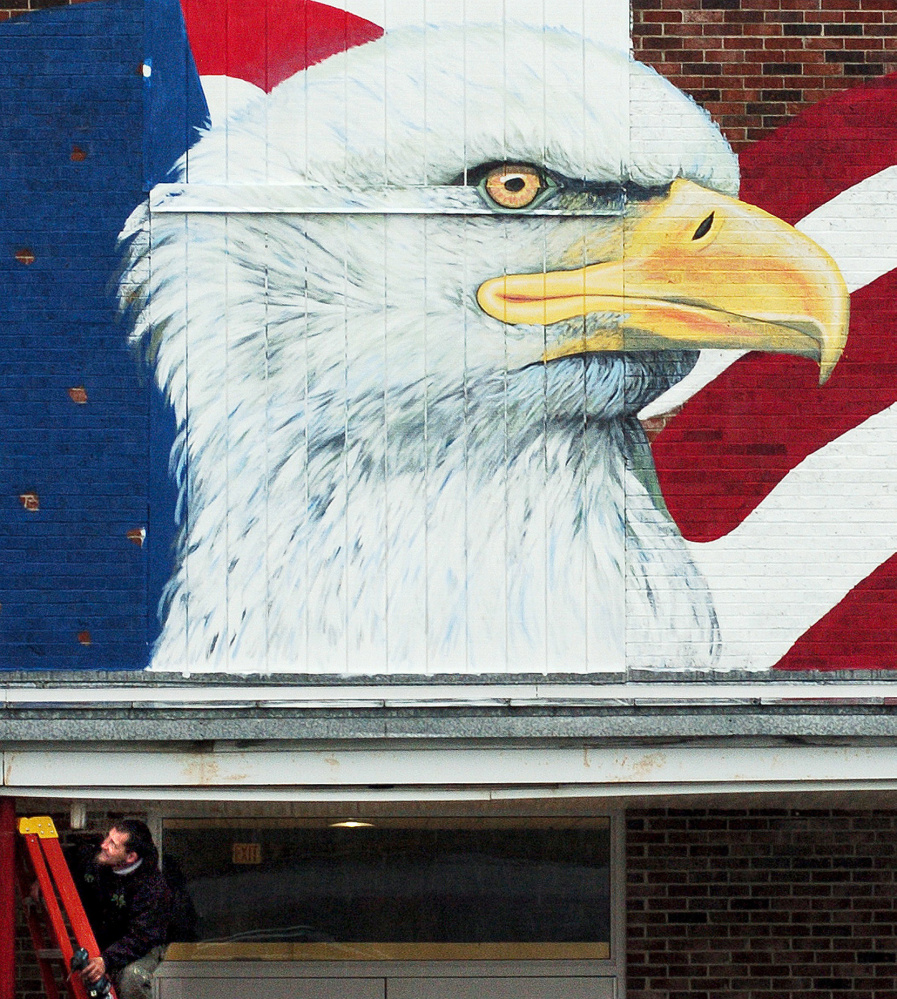 Worker Gary Page adjusts a drain for water Thursday on the canopy of the Skowhegan Village plaza building where a large mural showing an American flag and an eagle is being painted outside the Maine Veterans Museum that is under construction.