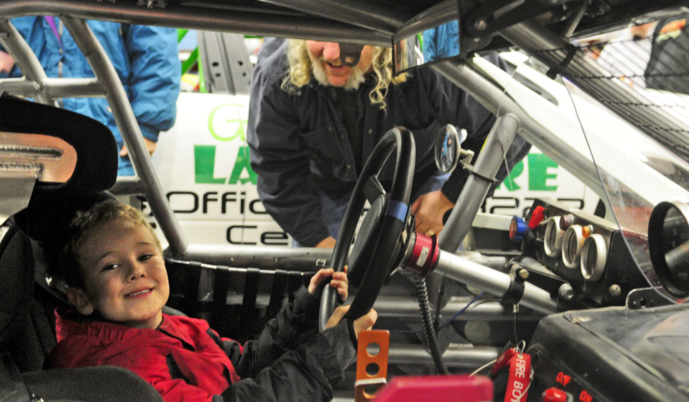 Staff photo by Joe Phelan 
 Ashton Doolan, 5 of Morrill, left, tries out a Tour Modified class car raced by Bill Dixon, top right, during the Northeast Motorsports Expo on Saturday at the Augusta Civic Center.