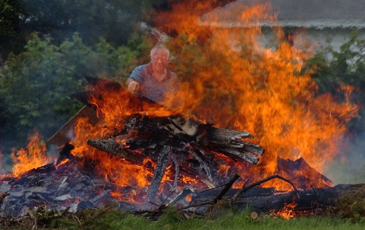 Steve Davis throws wood from an old building onto a burning pile behind his home on Lower Ridge Road in Fairfield.