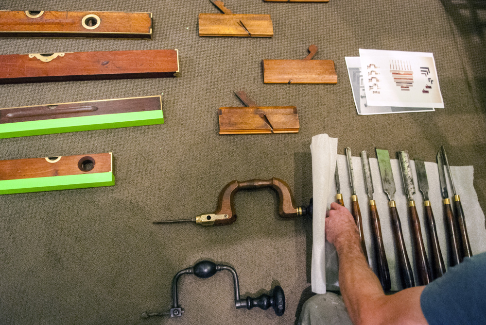 Staff photo by Joe Phelan
Ryan Walker, an exhibits preparator at the Maine State Museum, arranges chisels while building a display Tuesday in the entryway to the "Thos. Moser: Legacy in Wood" exhibition under construction at the museum in Augusta.