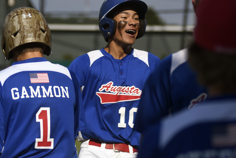 Augusta's Akira Warren is greeted by teammates after scoring the first run of the Babe Ruth 14U state championship game against Tri-County on Monday in Augusta.