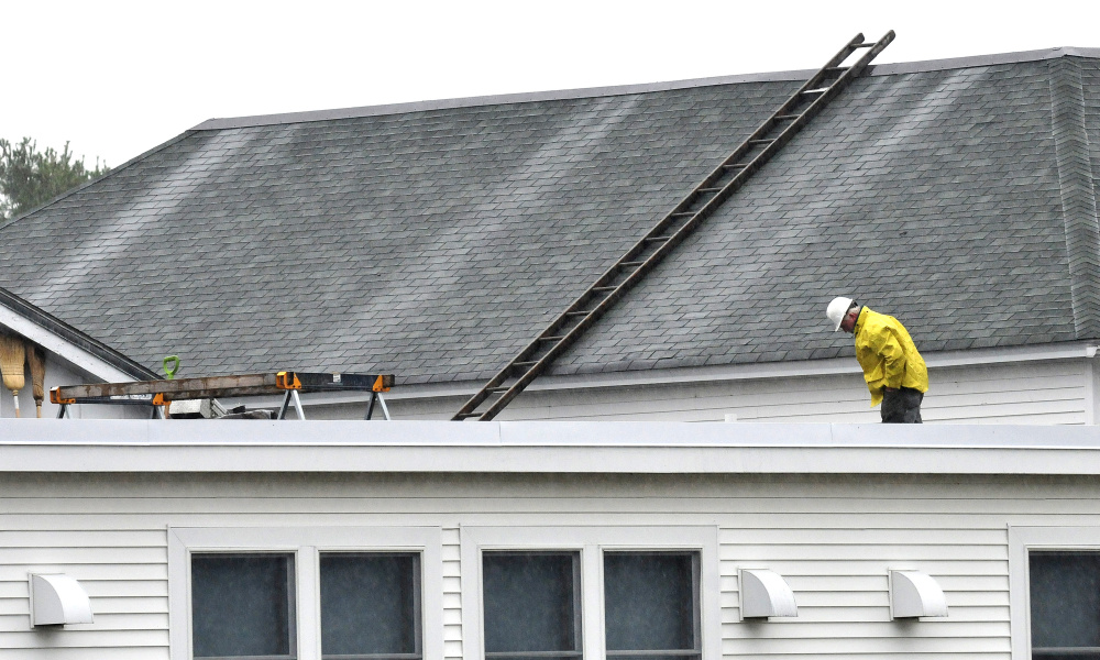 A worker surveys the roof of China Middle School after roots penetrated older drain pipes causing Tuesday evening's rain water to back up Wednesday.