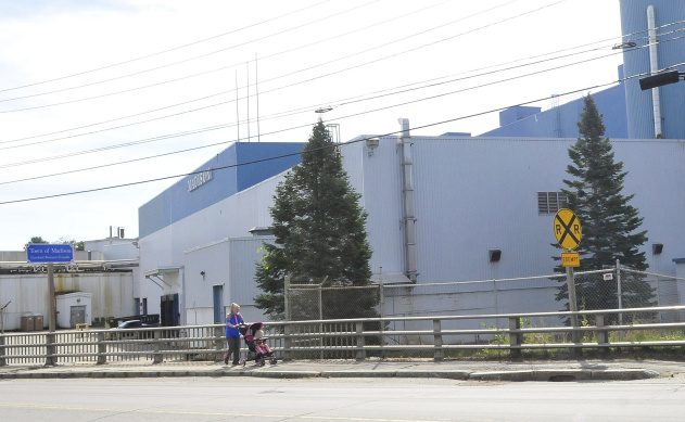 A woman and baby walk past the front of the shuttered Madison Paper Industries mill near a town "business friendly" sign on Thursday. The town is suing the owners of the former mill for information regarding property values.