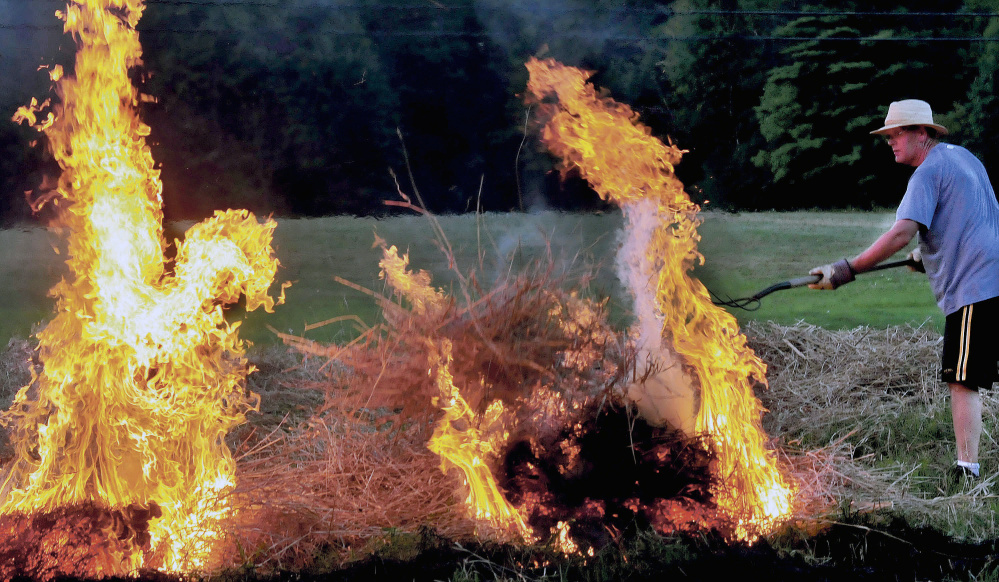 Peter Clifford throws a pitchfork full of burning brush to ignite another pile while he and his father, Roger, burn a field in 2014 in Benton. Even though legislation that passed earlier this year authorizes the issuance of burn permits by private online websites that municipalities have hired to do that work, the state Department of Agriculture, Conservation and Forestry continues to discourage their use.