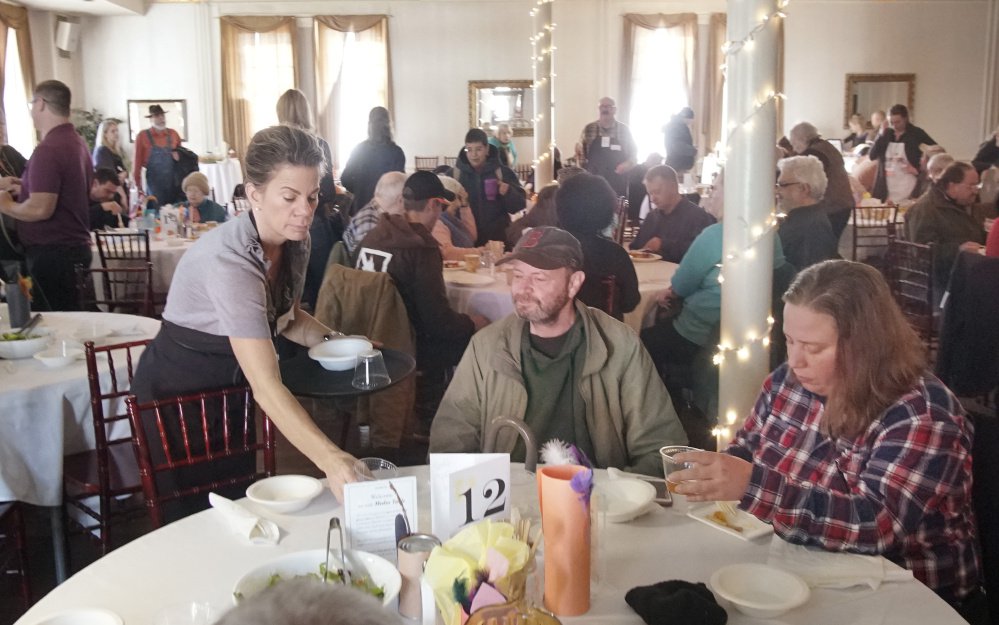 Volunteer Barbara Bhutto clears a table, while Jeffrey Dubois and Aimee Howard finish their Thanksgiving Day meal.