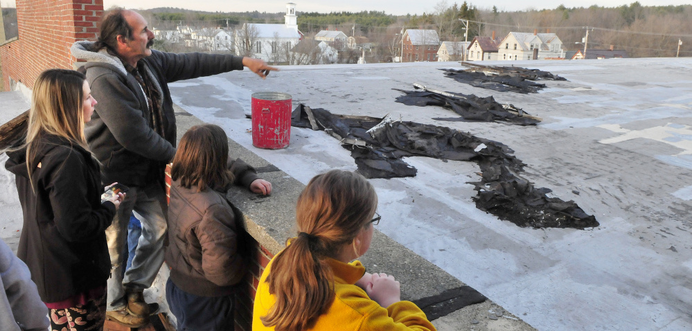 Ray Breton, owner of the Olde Mill in Vassalboro, points on Tuesday to an area where roofing was peeled off the roof of the mill by an Oct. 30-31 wind storm. At left is Kimberly Kimball, who on Dec. 2 is hosting one of many fundraising efforts to help raise $250,000 to repair the roof damage.