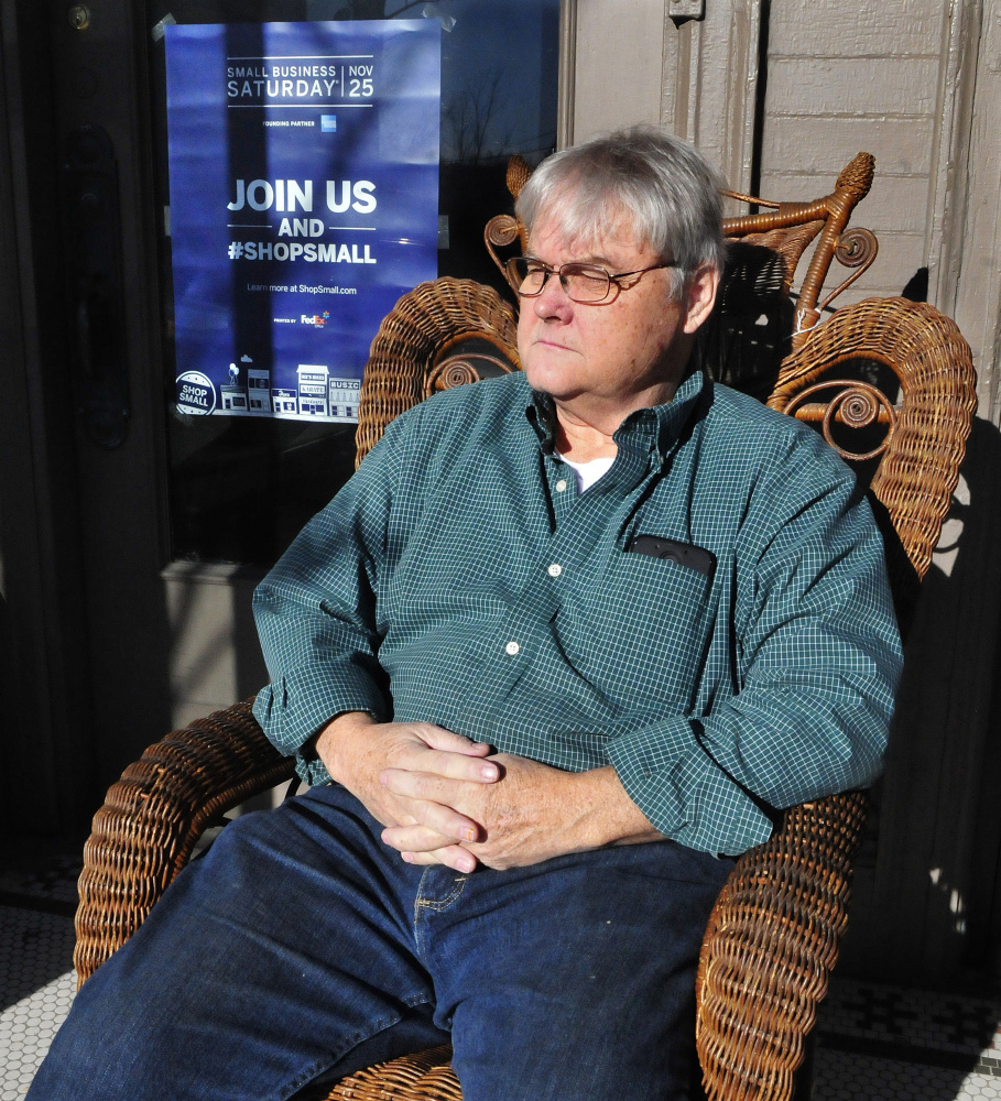 Downtown merchant Greg Salisbury relaxes on Tuesday in a chair outside his Hilltop Antiques store in Skowhegan after he put up a sign for this weekend's Small Business Saturday event.