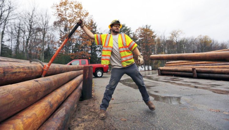 Central Maine Power Co. worker Jason Valera loosens a utility pole from a pile before it's lifted onto a trailer in Brunswick on Monday.