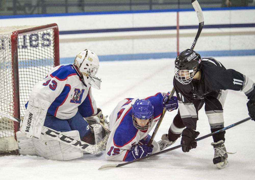 Kennebec RiverHawk defenseman Logan Denis (11) tries to push the puck past Messalonskee goalie Eli Michaud as teammate Reilly Benecke tries to defend during the first period of a recent Class B North game at Colby College in Waterville.