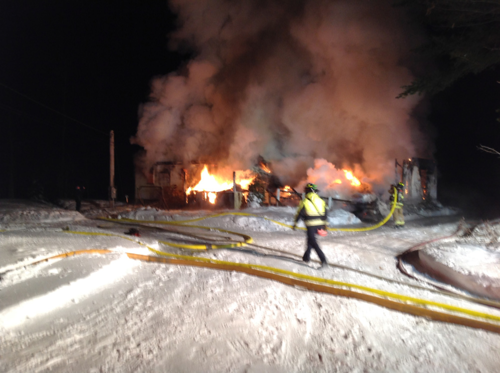 A firefighter walks along the hoses sending water to fight a fire Tuesday night at 58 Outlet Road in Augusta.