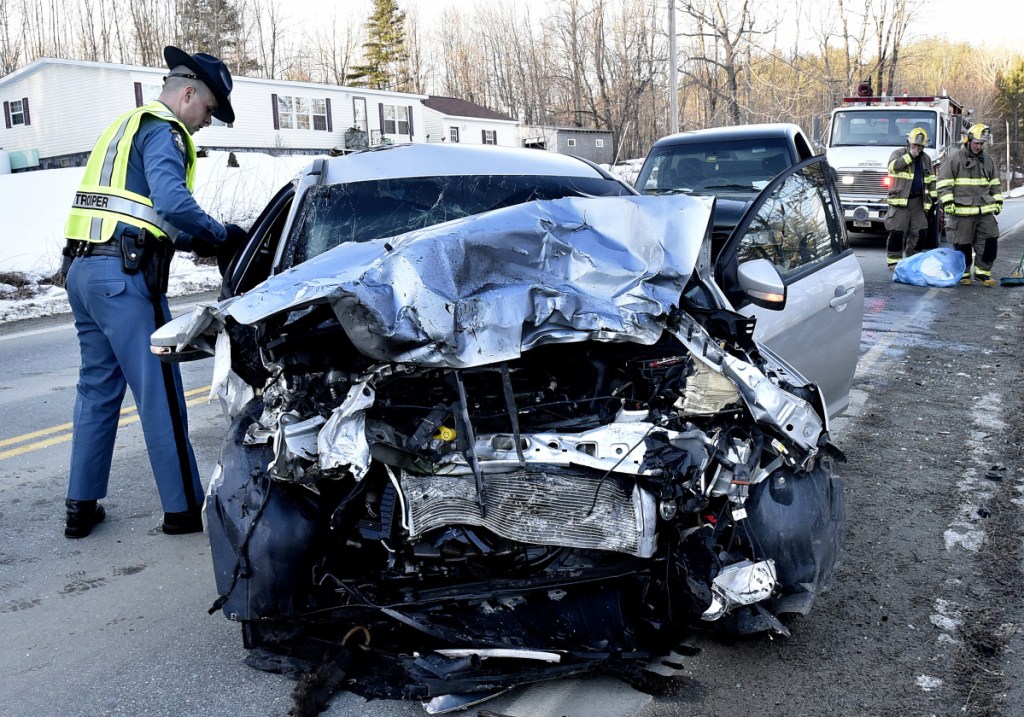 Trooper Jacob Roddy gathers evidence Monday from a demolished vehicle involved in an accident with a truck, background, on West River Road in Sidney. The roadway was blocked.