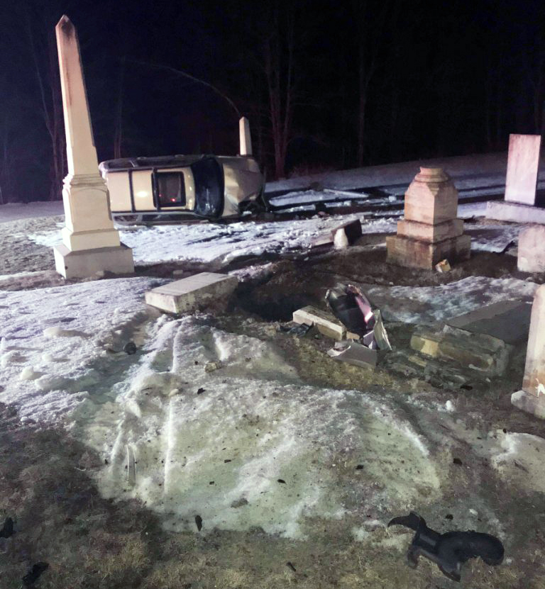 A 2006 Subaru Forester rests on its side following a crash early Tuesday, March 27, 2018, that left one woman injured and damaged a fence and toppled headstones at a cemetery next to St. Denis Church in Whitefield.