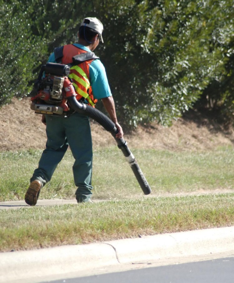 A landscaper blows clippings off a sidewalk.