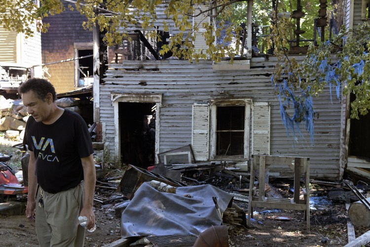 Tom Bustos walks by the burned-out remnants of his barn and home Sunday in Gardiner. Fire heavily damaged his family's Deane Street home Saturday night.