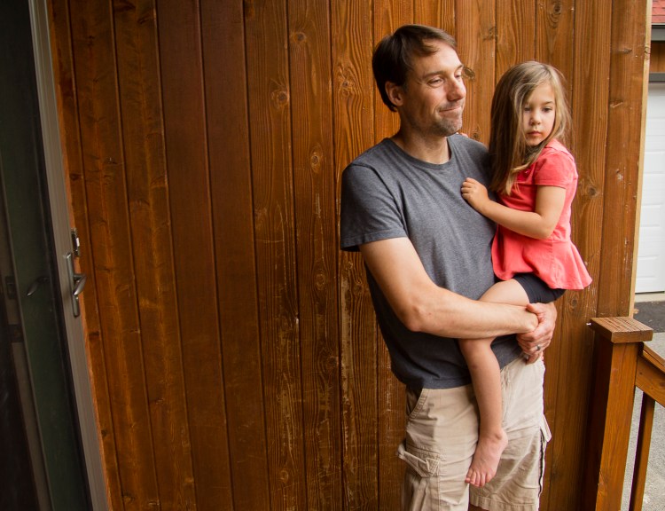 Alex Hallet, with daughter Sybil, talks Monday about witnessing and photographing the fox that came through his yard and also bit at least three of his neighbors on Friday. He was aware of the fox’s biting activity in the neighborhood and had his children and pets safely inside when he photographed it from an upstairs window. 