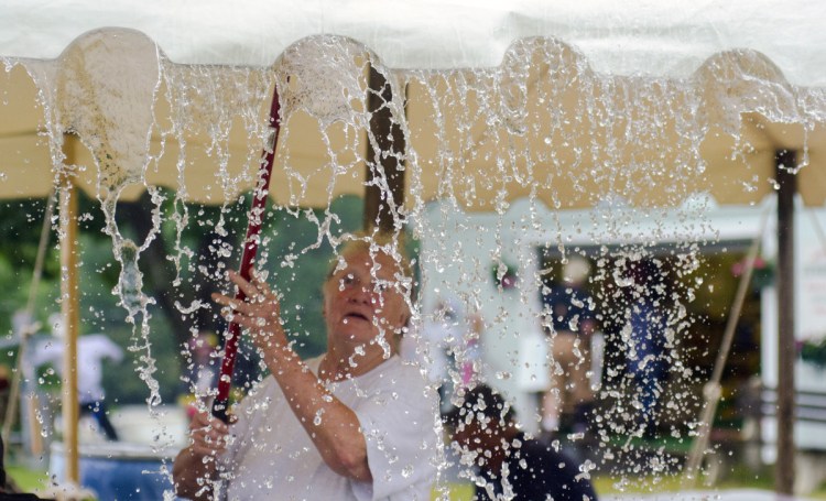 Fair volunteer Charlotte Kemp uses a broom to clear water that puddled in a tent over concession stand picnic tables Saturday at the Monmouth Fairgrounds.