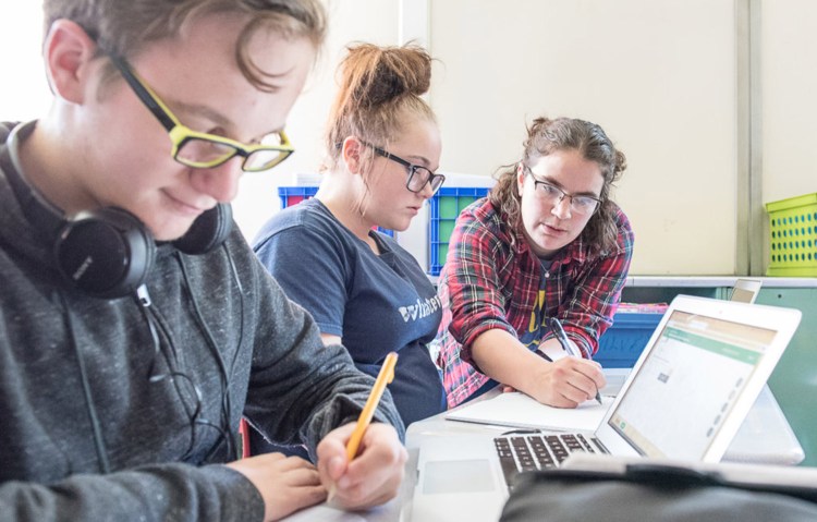 Noah Tirado works on an equation while freshman math teacher Ursula Cote, right, helps Zoe Collins on an assignment in math class at Edward Little High School in Auburn on Wednesday. The school has returned to a traditional grading system.