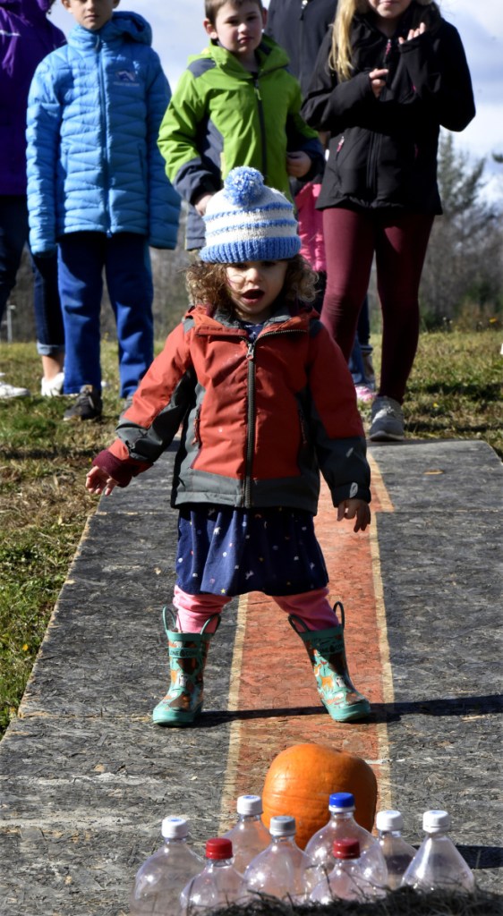 Nitzan Isaacs-Weiss watches the pumpkin she rolled head to some set up bottles during one of the kids events during the Quarry Road Trails Fall Festival in Waterville on Sunday.