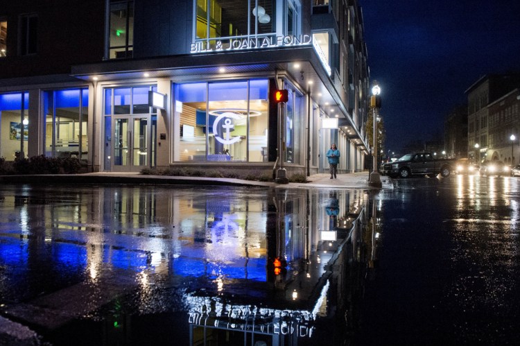 The newly constructed Bill & Joan Alfond Main Street Commons reflects in the water at the intersection of Temple Street and Main Street at night in Waterville on Nov. 1. Camden National Bank recently moved into the new downtown location.