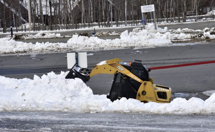 A worker clears snow Monday from one of many empty parking lots at Sugarloaf in Carrabassett Valley. 