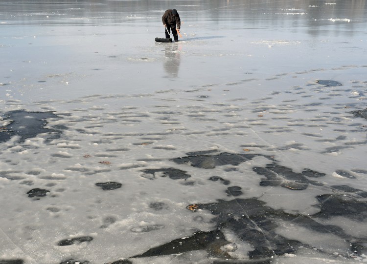 Rob Angelides, of Lewiston, collects a trap while ice fishing Sunday on Cochnewagon Pond in Monmouth. Cool temperatures have drawn anglers to the ice, which game wardens caution is still very thin on many bodies of water. Angelides said he caught a few small trout and cut through 6 inches of ice to put out his trap.