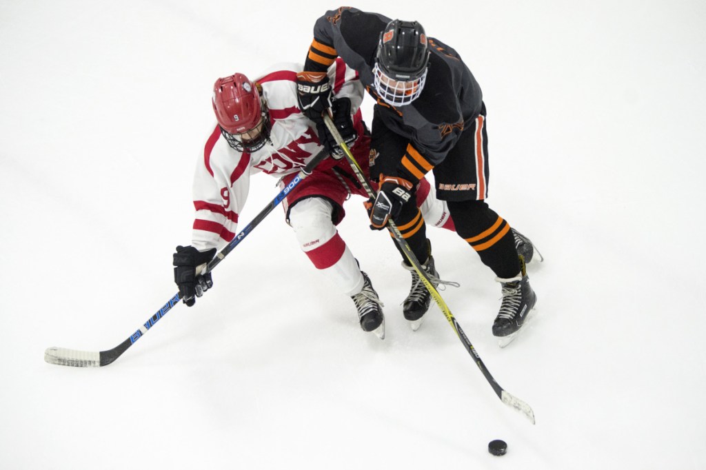 Cony's Vinny Manocchio, left, battles for the puck with Brunswick's Henry Burnham last week at the Camden Nation Bank Ice Vault in Hallowell.