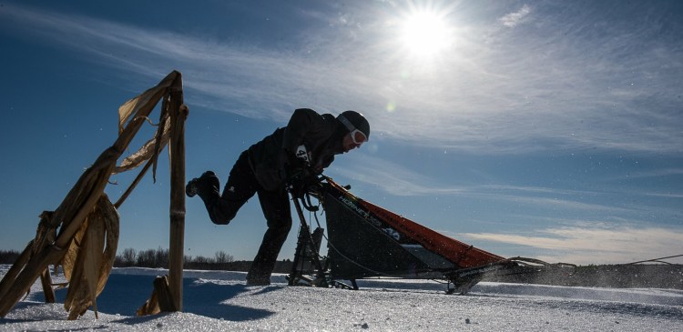 Jean Rene Saucier, of Woburn, Quebec, pushes his sled through a frozen cornfield in Farmington on Sunday in Maine State Sled Dog 8-team Race.