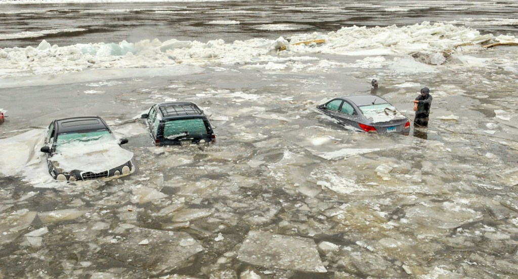 Kameron Knowles, of AC Towing, rolls up his sleeves before reaching into the cold water to hook a tow cable onto Stephanie Arnio's 2014 Hyundai Accent on Jan. 15, 2018, in a riverfront parking lot at the end of Central Street in Hallowell. Arnio, who lived in a downtown apartment nearby, said they were surprised to wake up Sunday morning and see the Kennebec River covering vehicles.