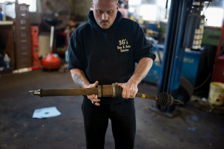 Bob Byrnes at 3G's Tire and Auto in Portland holds an axle he removed Tuesday from a car that was brought in with a damaged bearing after it hit a pothole. The bearing is about a $400 repair. Josh Byrnes, the manager of the shop, said about 15-20 cars per week are brought in because of pothole damage.