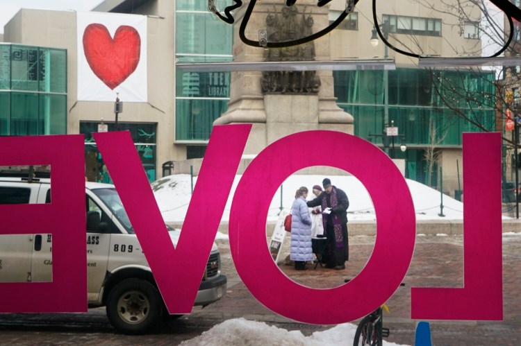 In 2018, Valentines Day fell on Ash Wednesday, the start of the Lenten season for Christians. Pastor Larry Weeks prays with Amy Anderson in front of the Portland Public Library, with its large heart banner, hung by Valentines Day phantoms. Gregory Rec/Staff Photographer
