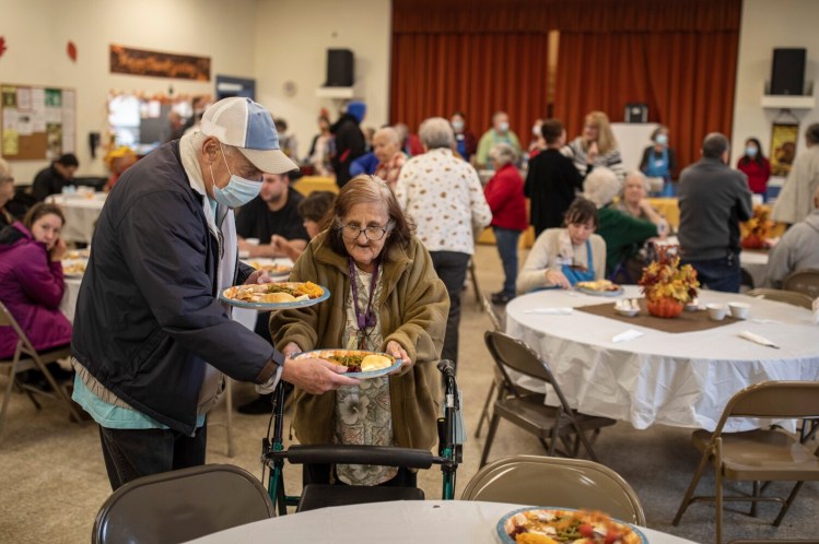 SACO, ME - NOVEMBER 25: Ted Walogorsky helps Betty Durbetaki set her meal down at their table at the Good Shepherd Parish and the Knights of Columbus 22nd Free Thanksgiving Dinner on Thursday, November 25, 2021 in the hall of Most Holy Trinity Church. Anyone from the community was invited to attend. Dozens of volunteers served hundreds of meals, as well as delivering several hundred more Thanksgiving meals. Walogorsky has been coming to the dinner for twenty years, he and his partner Sherri Laux are neighbors of Durbetaki, and now they all come together. (Staff photo by Brianna Soukup/Staff Photographer)