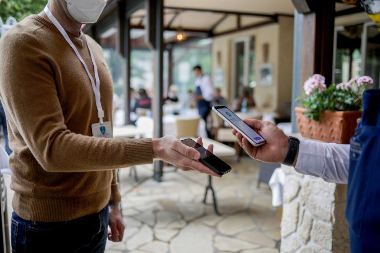 The CovPass Check app, right, is used by a worker to scan a customer's bar code from the CovPass app, inside a restaurant arranged in Berlin on Aug. 23, 2021. MUST CREDIT: Bloomberg photo by Liesa Johannssen-Koppitz.