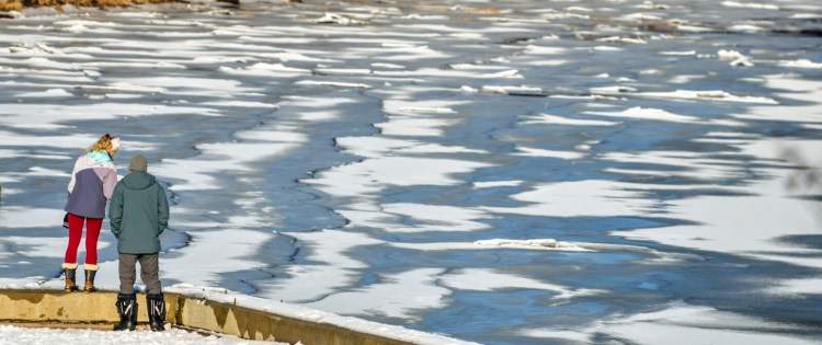 People look out over the patterns of snow on the ice on the Kennebec River on Dec. 31, 2021, from the bulkhead in  Hallowell's Granite City Park. 