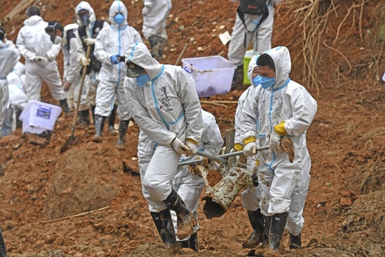 Rescuers carry a piece of plane wreckage at the site of Monday's plane crash in southern China's Guangxi Zhuang Autonomous Region on Friday. Construction excavators dug into the crash site Saturday in the search for wreckage, remains and the second black box from a China Eastern 737-800 that nosedived into a mountainside with 132 people on board. 