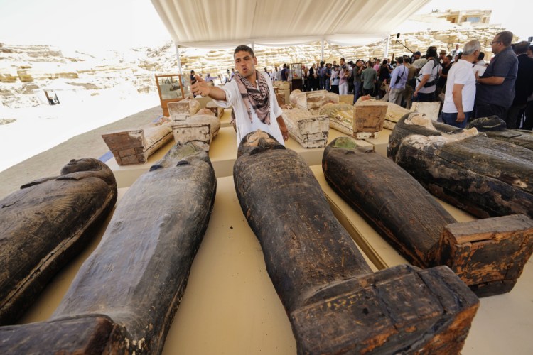 An antiquities employee tries to prevent reporters from getting close to painted coffins with well-preserved mummies inside, at a makeshift exhibit at the foot of the Step Pyramid of Djoser in Saqqara 15 miles southwest of Cairo on Monday. (AP Photo/Amr Nabil)