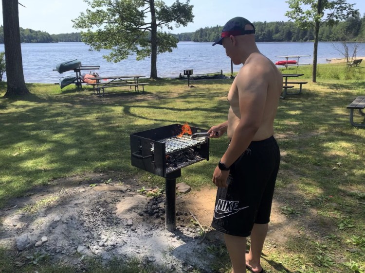 Mhamed Moussa Boudjelthia, of New York City, works a grill Sunday at Promised Land State Park in Pennsylvania's Pocono Mountains in Greentown, Pa. He and friends came to escape the heat in the city. Residents around the Northeast braced for potentially record-breaking temperatures Sunday as a nearly weeklong hot spell continued. 