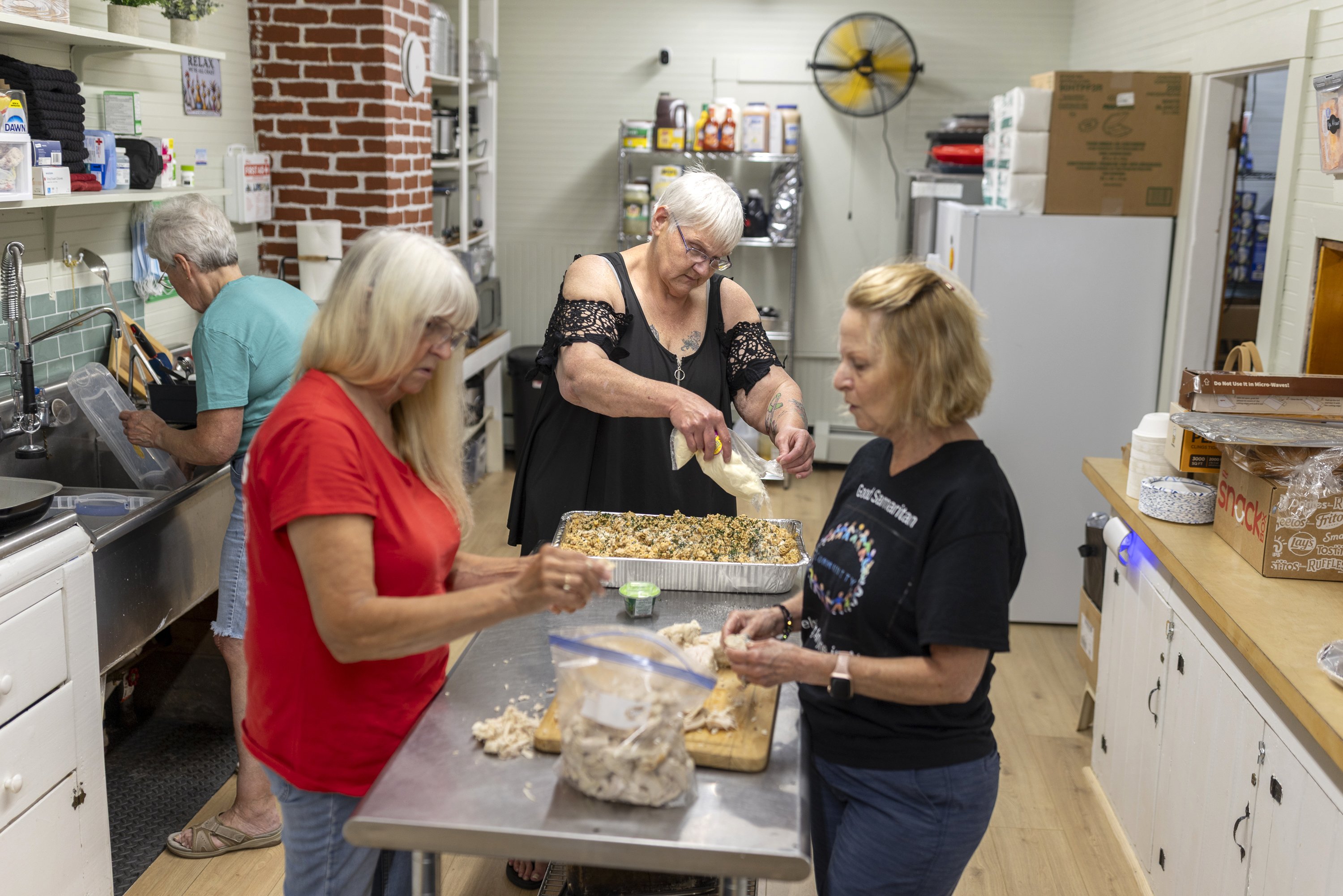 Four women stand in a kitchen preparing a meal. One is washing dishes.