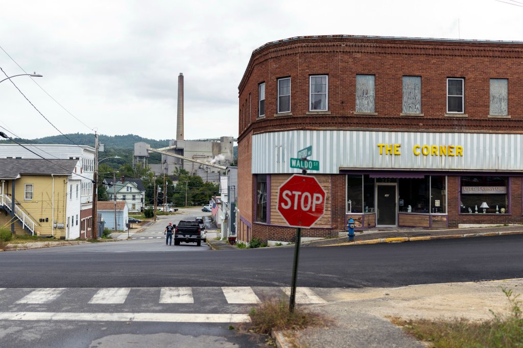 The intersection in front of a business named The Corner. In the foreground is a stop sign and the Waldo Street sign. In the background is a smoke stack from an industrial building.