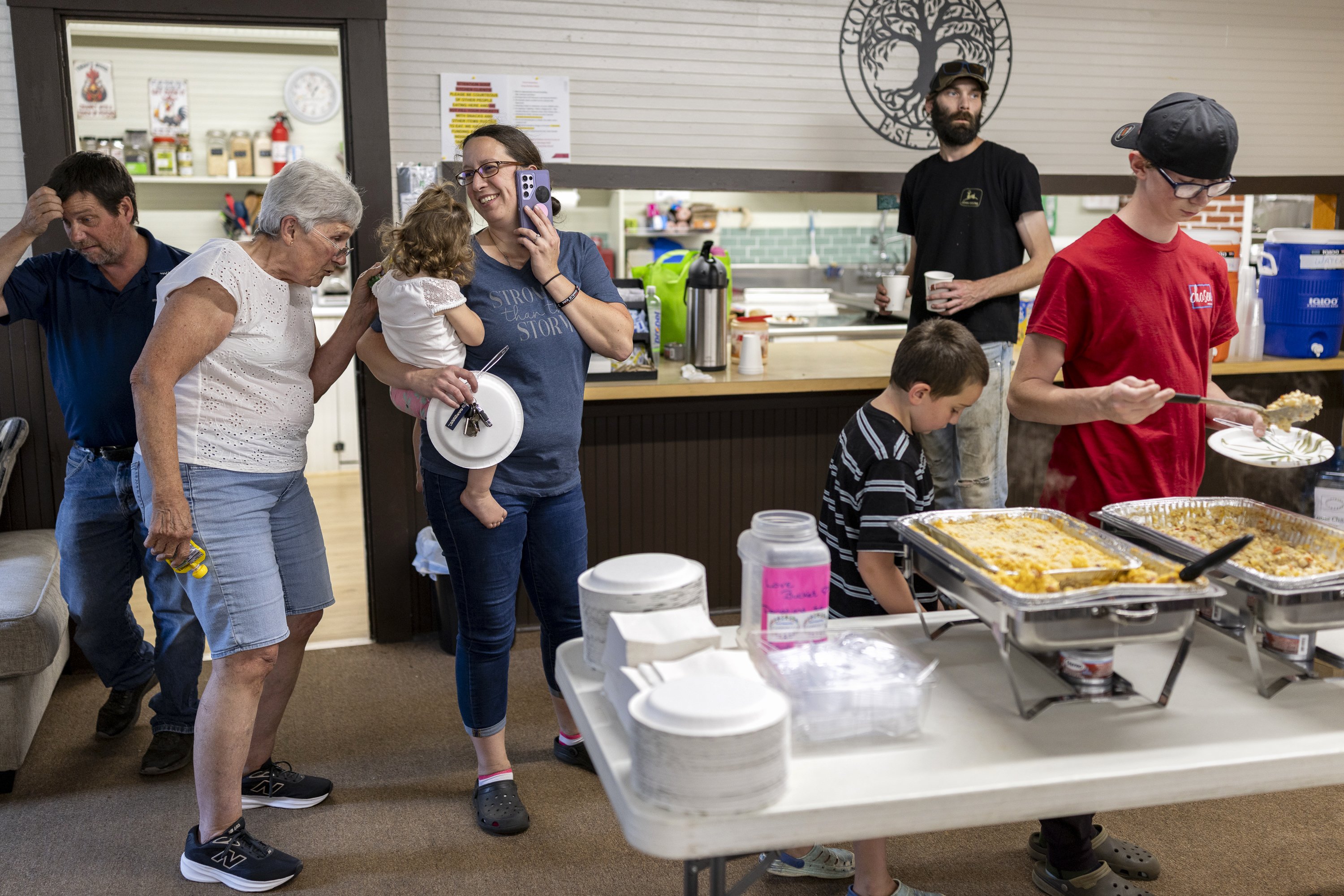 People line up for food from a table with pasta dishes.