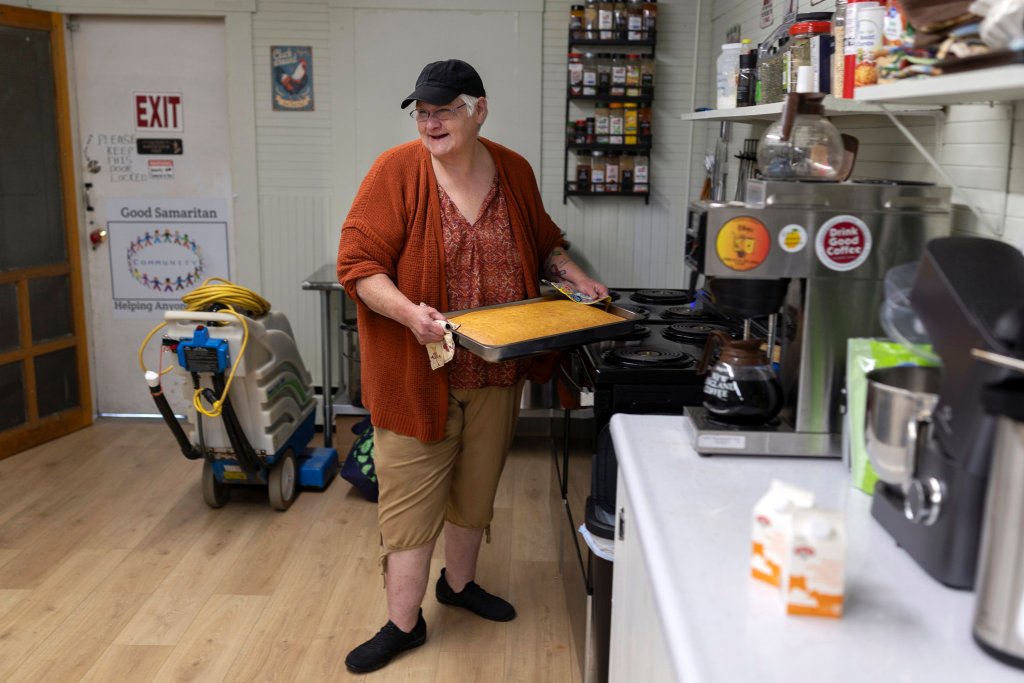 A woman in a baseball cap holds a yellow cake in front of a stove